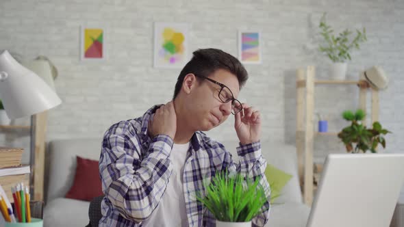 Young Asian Man in a Shirt with Neck Pain Sitting at the Laptop