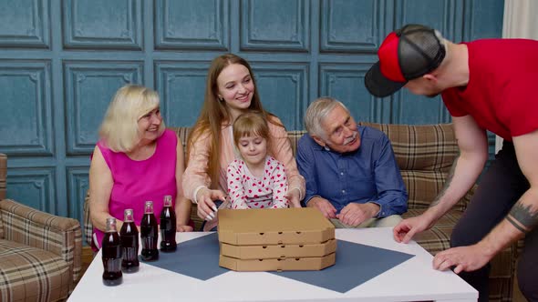 Delivery Man with Fast Food Boxes Puts Hot Pizza on Table in Front of Large Multigenerational Family