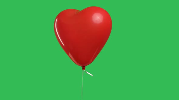 Red Heart Shaped Balloon Hanging in the Air Against the Background of a Green Screen Chroma Key