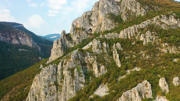 Aerial zoom out cave, rocky mountain with autumn forest trees on slope