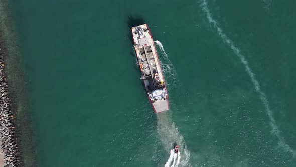 A large industrial dredge maneuvers in the water while a fast pilot vessel navigates beside the ship