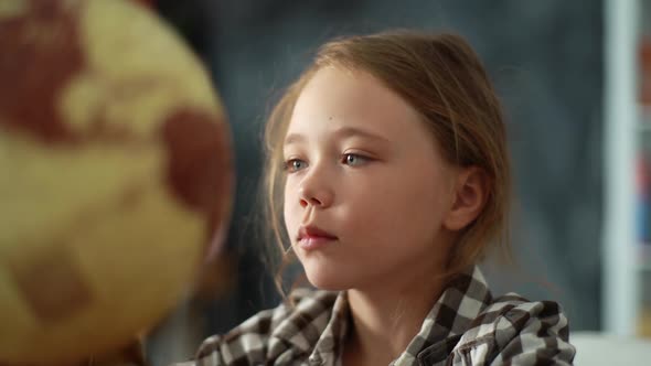 Closeup Face of Adorable Thoughtful Child Girl Spinning Small Globe with Interest Looking at