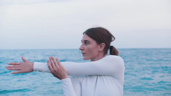An Adult Woman Doing Meditative Exercises on the Shore of the Sea