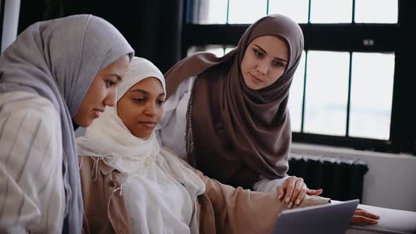 Three Muslim Girls Look at the Laptop Sitting on the Couch Smiling and Laughing