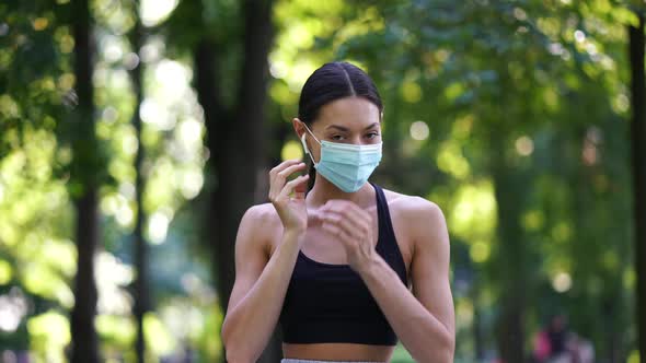 A Happy Woman in the Park Takes Off the Protective Face Mask