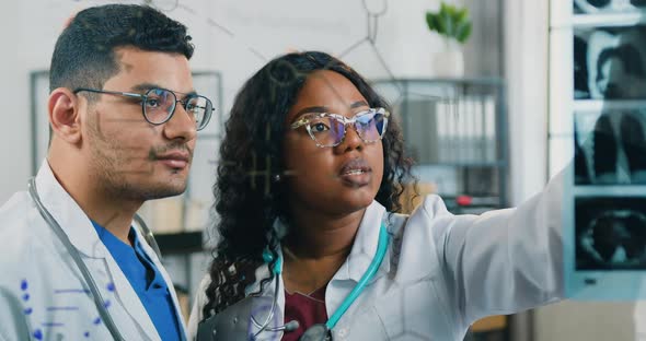 Doctors Discussing Between them Results of Patient's X-ray Scan that Attached to Glass Board in Lab