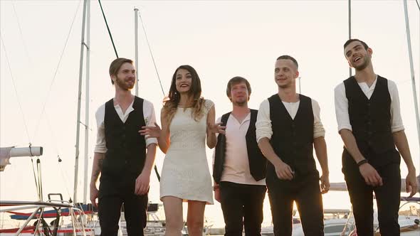 Company of Friends Who Look Like Musicians Stroll Along the Pier in the Evening