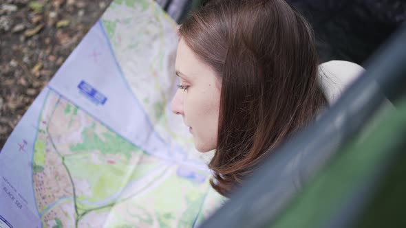 A Woman Traveler Studies the Map While Lying in a Tent