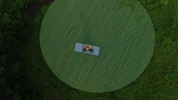 The girl does yoga outdoors in the field on the mat. Aerial view