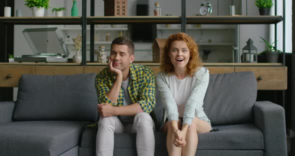 Young Couple Is Watching TV, Woman Is Excited, Man Is Bored