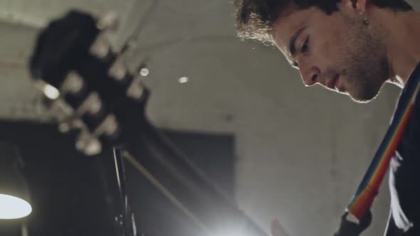 Side View of Young Modern Casual Man Playing Guitar While Standing in Studio with Microphone in Back