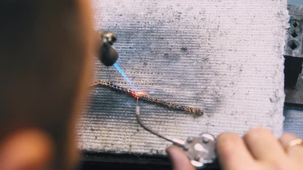 Worker Welds Gold Chain with Gas Burner and Tool on Sheet