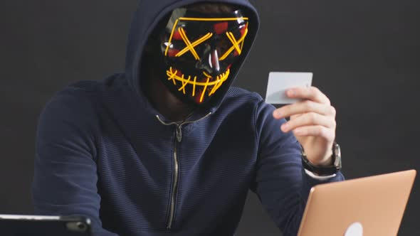 Masked Male Hacker Uses Laptop To Access Credit Card in Dark Office Room