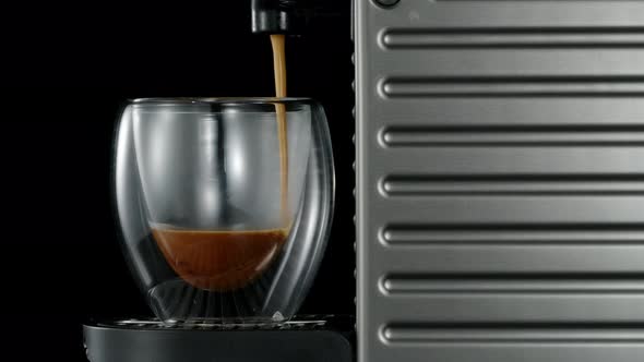 Black coffee machine pouring hot drink into the glass cup