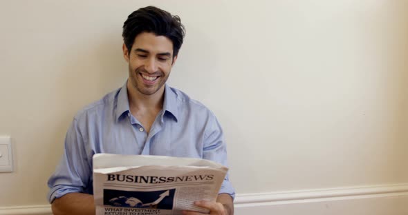 Smiling man reading business newspaper at home