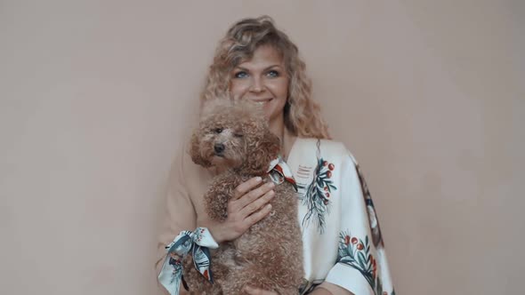 Beautiful Smiling Girl with a Poodle Dog in Her Hands and a Scarf Posing at Camera