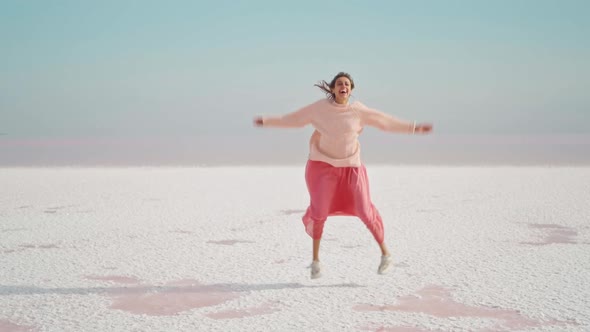 Attractive Happy Laughing Girl in Pink Oversize Sweater and Dress Funny Jumping on White Salty