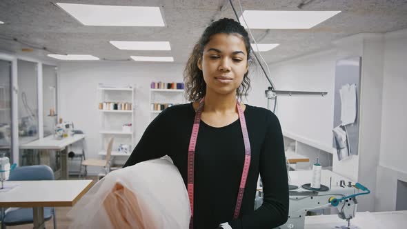 Young Africanamerican Woman Tailor or Fashion Designer is Holding Roll of Fabric and Smiling Posing