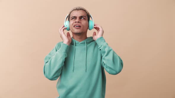 Pleased curly-haired man wearing blue hoodie listening music in headphones