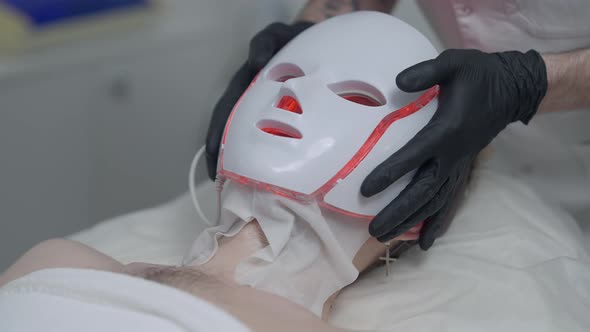 Closeup Putting on of Innovative Red LED Light Device on Face of Young Caucasian Man in Beauty