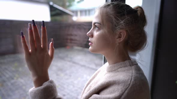 Side View Portrait of Sad Brokenhearted Teenage Girl Looking Out the Window on Rainy Day Touching