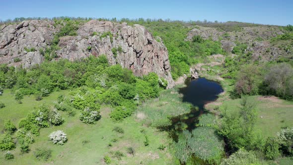 Aerial View of a Big Rock Formation and a Blue Pond Among the Greenery