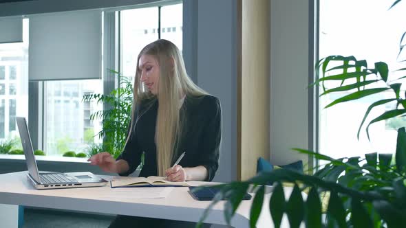 Elegant Woman Working in Stylish Office. Modern Blond Woman in Trendy Suit Sitting at Table in Light