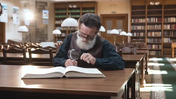 Old Man in Glasses which Recording Important Notes From the Book, Sitting in the Library