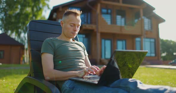 Focused Young Man Working at Laptop in Courtyard of Country House