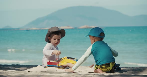 Children Play with a Plastic Crane and a Car on the Sand at the Beach