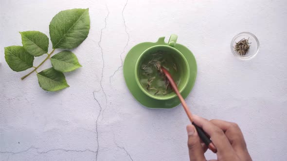 Hand in Spoon Mixing Herbal Leaf with Hot Water