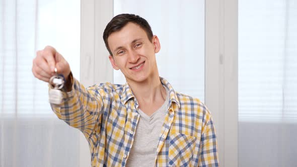Smiling Man Shows Keys with House Breloque Near Window