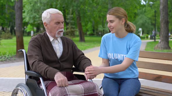 Pretty Female Volunteer Supporting Aged Male Patient in Wheelchair