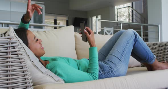 Mixed race woman lying on couch having video chat on smartphone blowing kisses