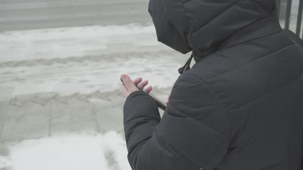 Falling Snow Woman in Warm Jacket By the Roadside Calls Taxi Through Her Phone