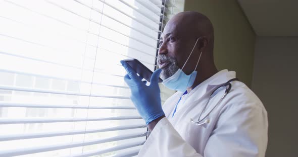 Portrait of african american male doctor wearing face mask talking using smartphone