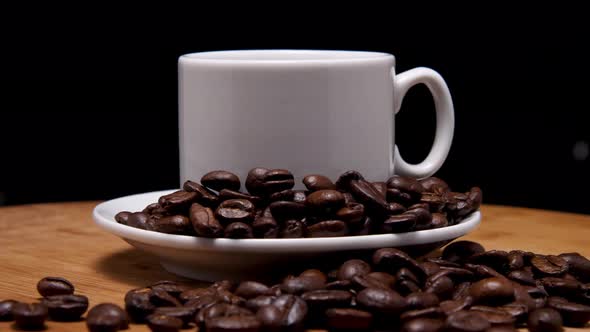 Close-up of a white mug and saucer with coffee on a wooden background. Roasted arabica coffee beans