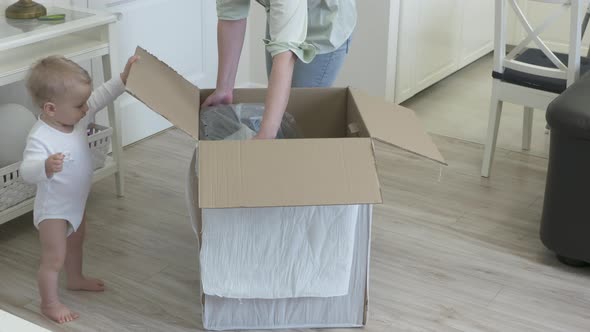 Woman with Baby Unpacking Unboxing Large Cardboard Package Box at Home Parcel with New Child Car