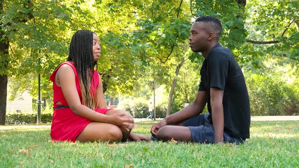 A Black Man and a Black Woman (Young and Attractive) Sit on Grass and Talk in a Park on a Sunny Day