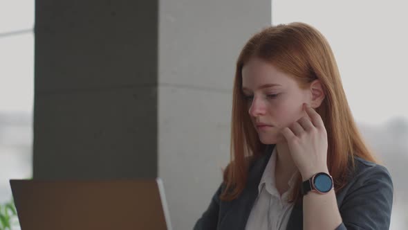 Thoughtful Concerned Redheaded Woman Working on Laptop Computer Looking Away Thinking Solving