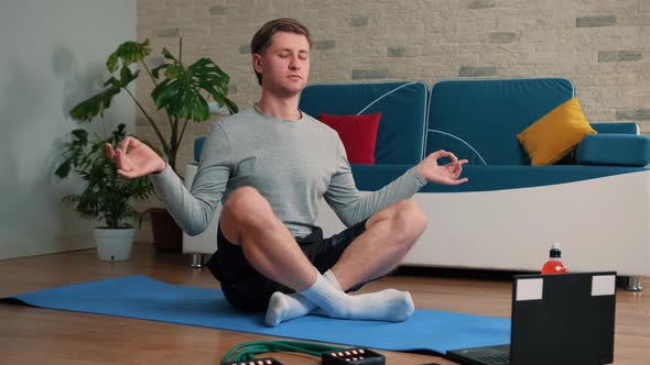 Young Man Meditating in Lotus Pose on Exercise Mat at Home