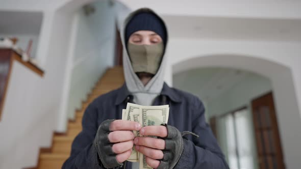 Blurred Burglar in Mask Counting Dollars Standing in Wealthy House Indoors