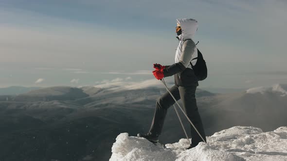 A Young Woman is Standing on the Edge of a Snowcovered Cliff and Looking at the Landscape