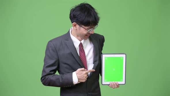 Young Happy Asian Businessman Showing Digital Tablet To Camera and Pointing Finger