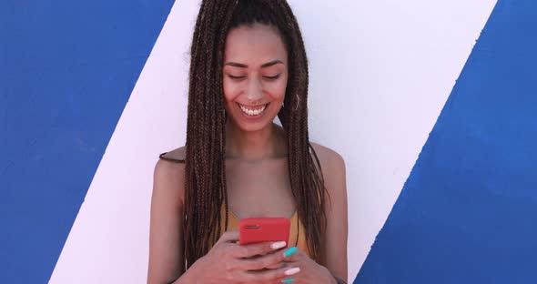 Bohemian mixed race young woman using smartphone outdoor with colorful background