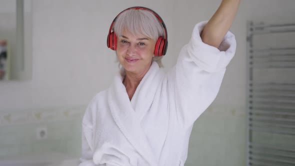 Front View Portrait Cheerful Mature Woman in Headphones Dancing in Slow Motion in Bathroom Looking