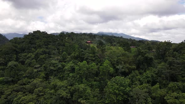 Drone orbiting around a mountain covered by thick rainforest and a hilltop building in central Ameri