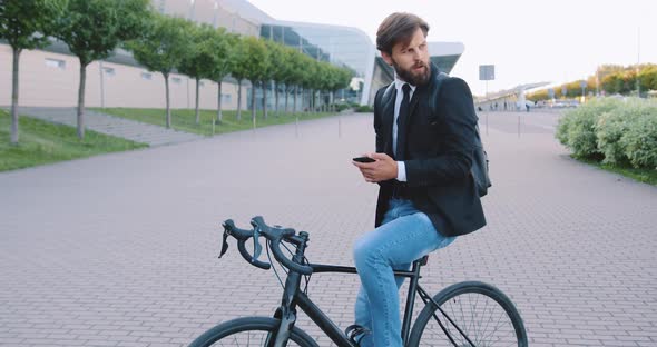 Office Worker which Sitting on His Bike and Using Phone on the Big Urban Building Background
