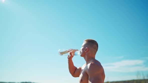 Muscular sportsman with a bottle of water in open air.