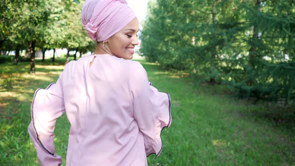 Young Muslim Woman in a Turban Runs in the Park and Turns Smiling